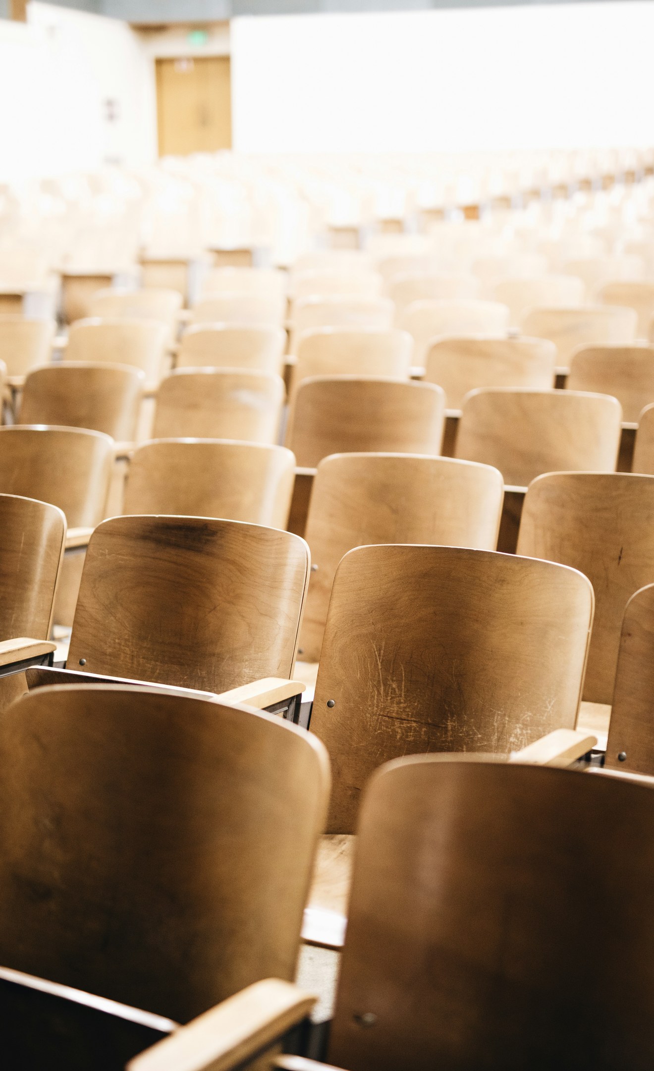Rows of empty wooden seats in a university lecture hall.