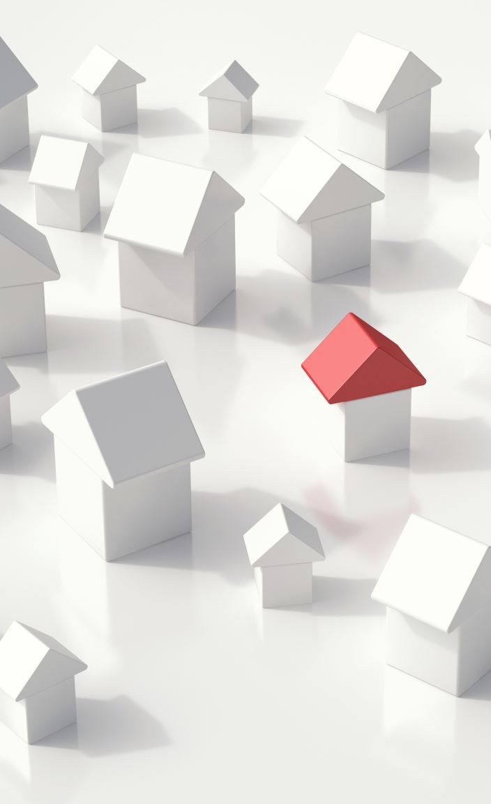 Dozens of small white model houses spread across a white surface, with one red-roofed house among them.