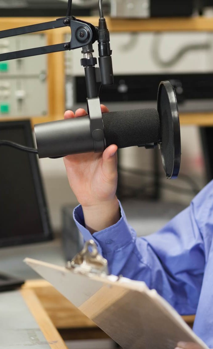 A radio presenter at a studio microphone, headphones on, mid-broadcast.
