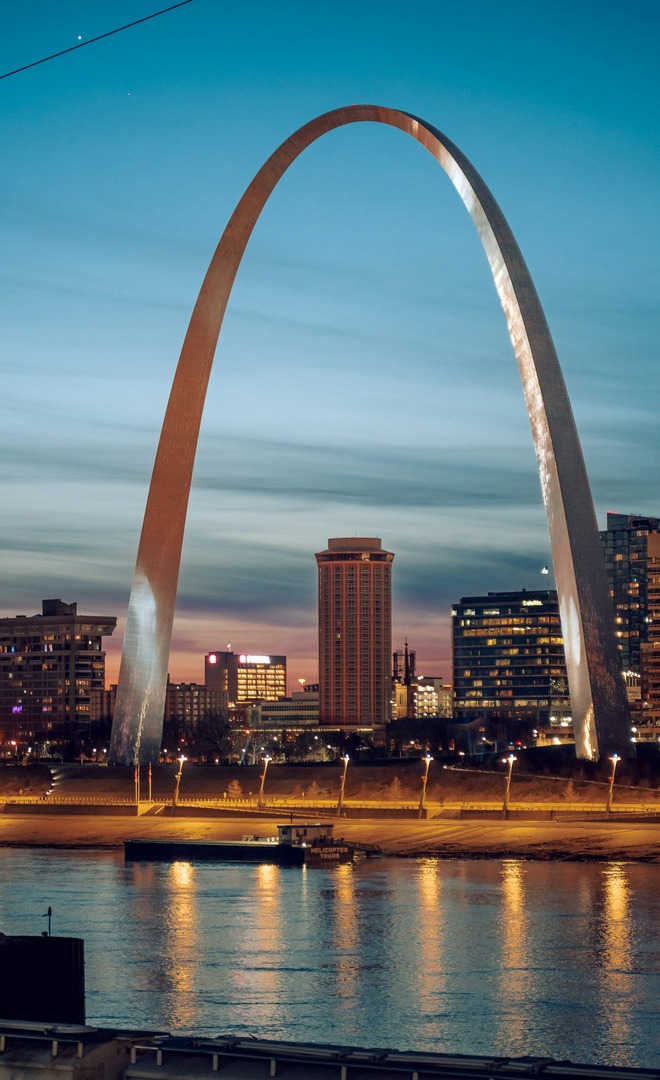 The Gateway Arch above the St. Louis skyline at dusk, reflected in the Mississippi.