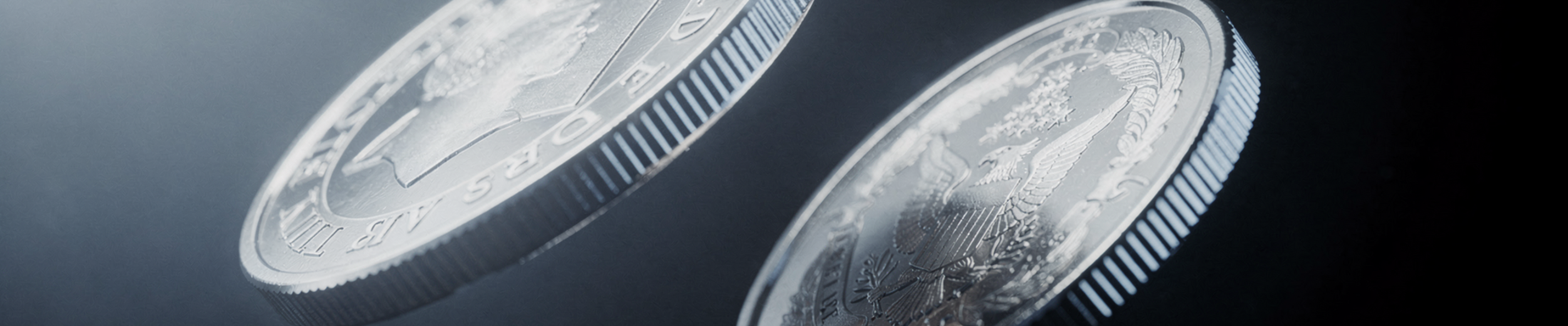 Two large silver coins in raking light against a dark background, one turned to show an eagle.