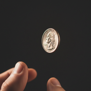 A hand flipping a quarter above a second, open hand, against a dark background.