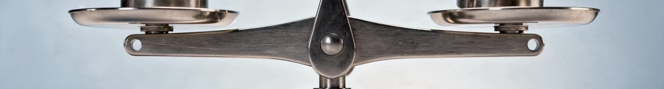 The polished metal beam and central pivot of a balance scale, its two pans hanging level.