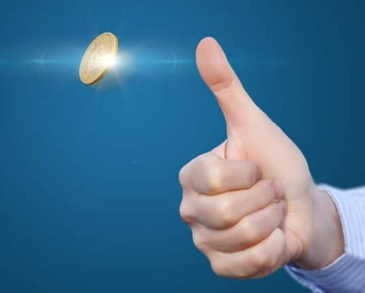 A gold coin spinning in mid-air beside a hand giving a thumbs-up, on a plain blue background.